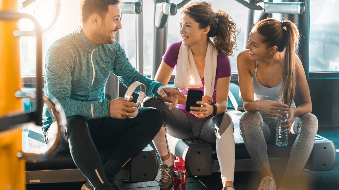 Tipps für erfolgreiche Lead Gen Kampagnen 2 Frauen und ein Mann im Fitnessstudio unterhalten sich fröhlich über eine App