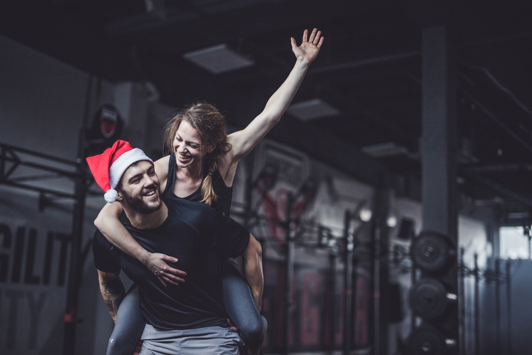 Young happy athletic couple piggybacking on New Year's day in a gym.